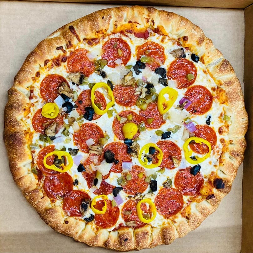 A DAIQUIRIS & DEAUX PIZZA pepperoni pizza with various toppings in a cardboard box.