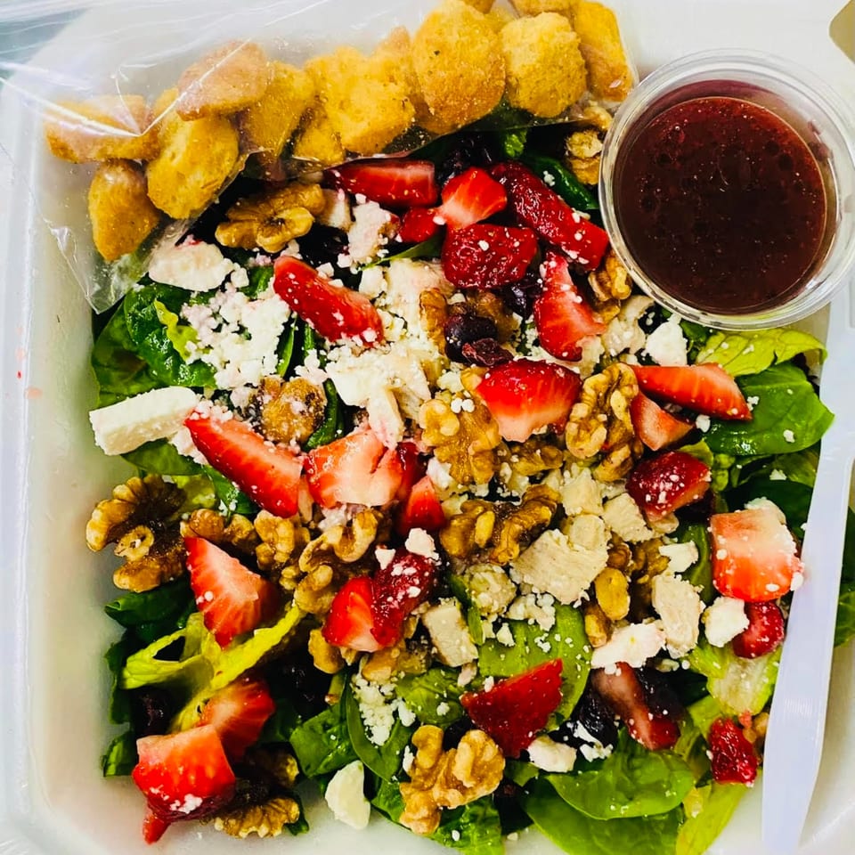 A vibrant spinach salad with strawberries, walnuts, feta, and croutons, with a side of dressing.