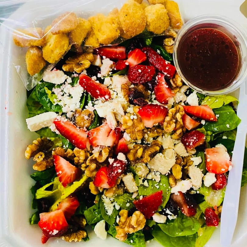 A vibrant spinach salad with strawberries, walnuts, feta, and croutons, with a side of dressing.