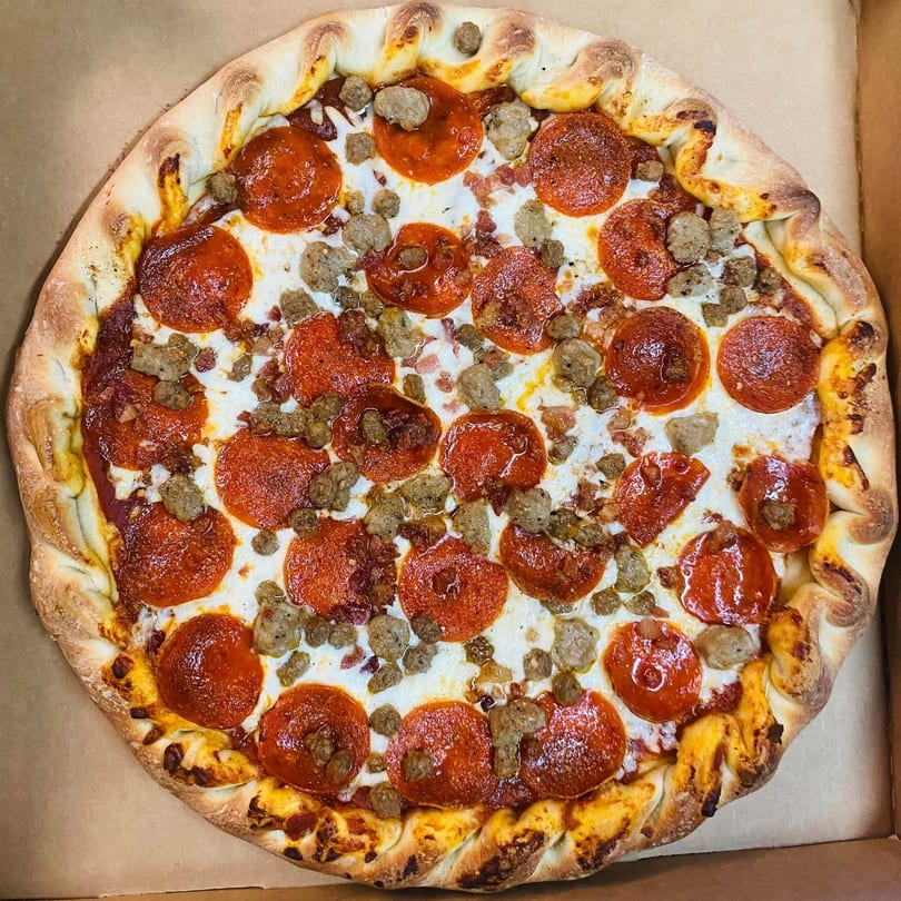 A DAIQUIRIS & DEAUX PIZZA pepperoni and sausage pizza with a braided crust in a box.