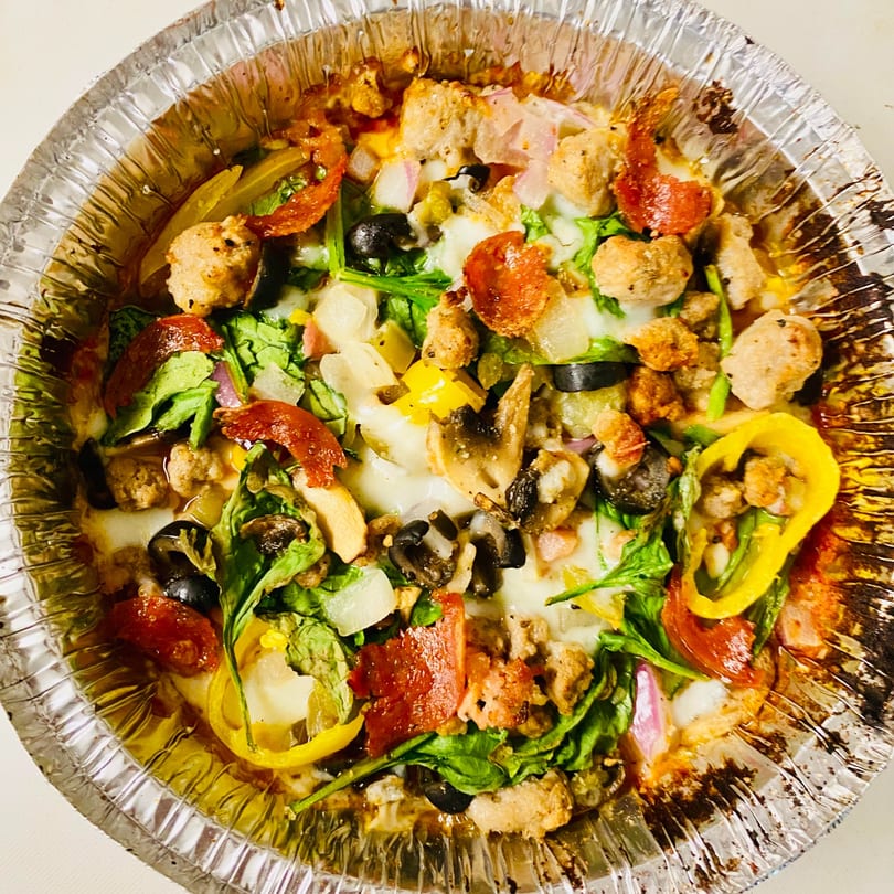 A close-up of a DAIQUIRIS & DEAUX PIZZA with various toppings in a foil pan.