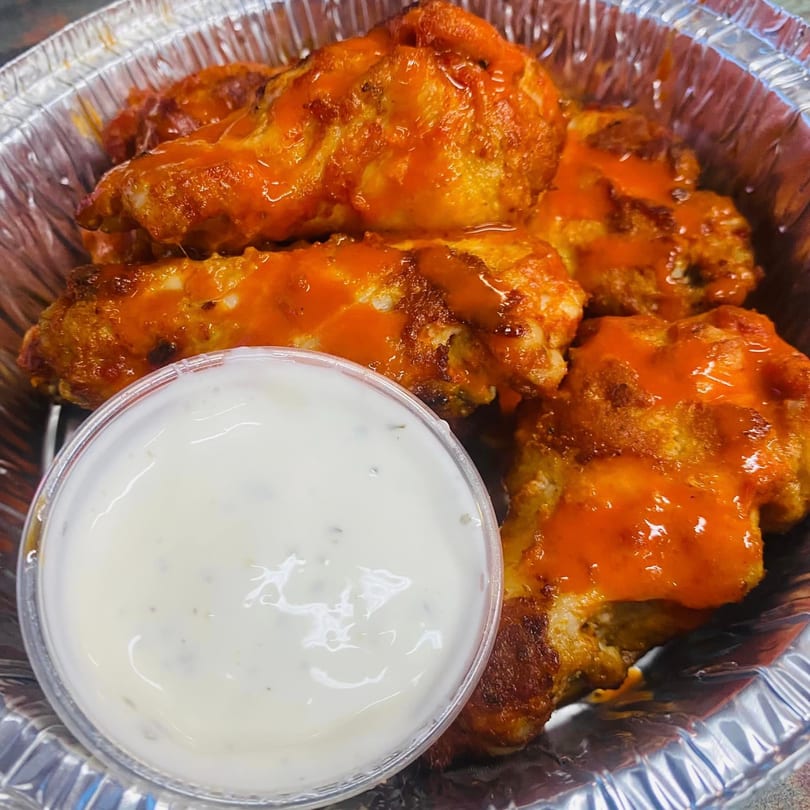 Buffalo wings with orange sauce and a side of ranch dressing in a foil container.